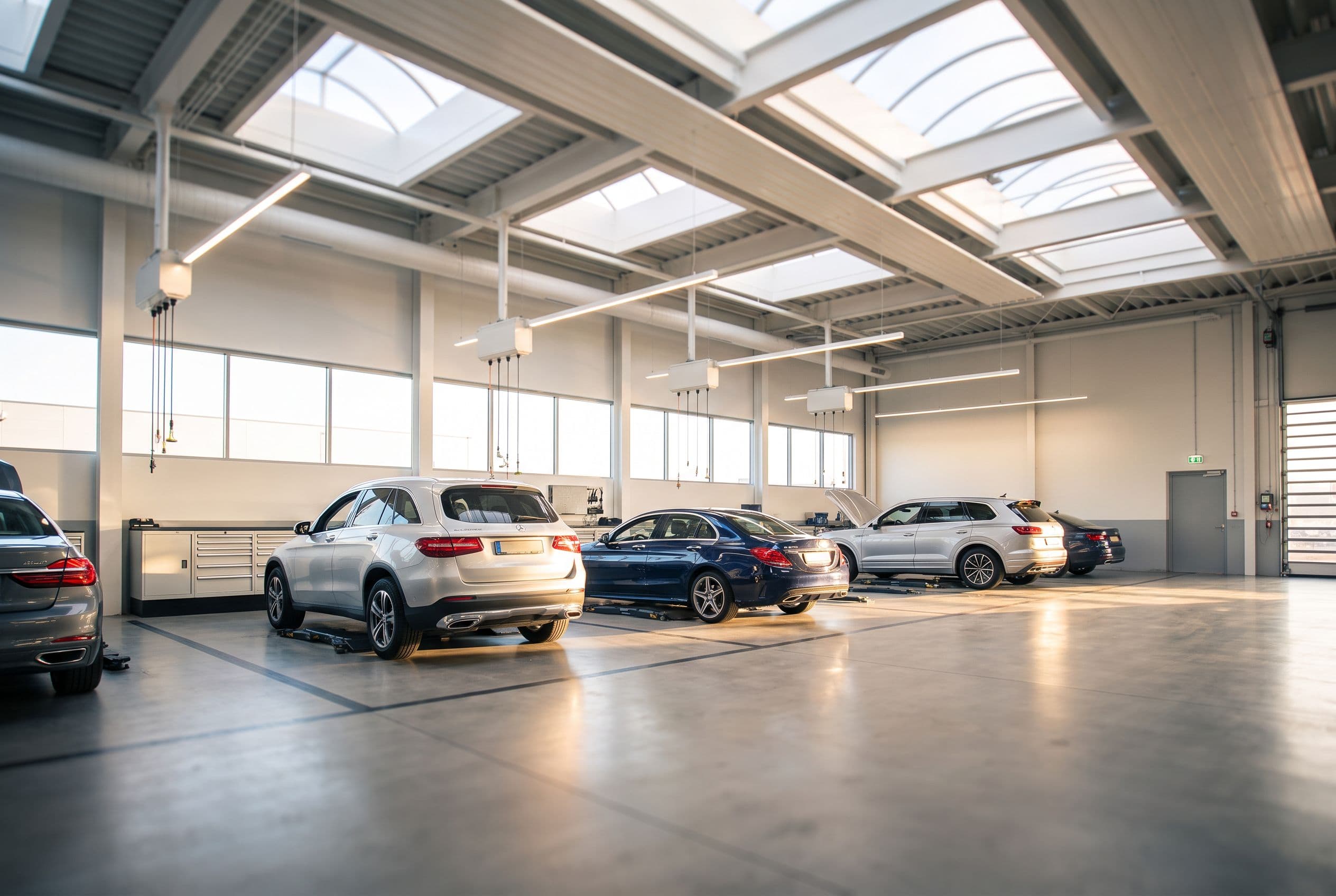 A larger dealer service department at dusk, a long row of bays under cool light, cars staged and moving through.